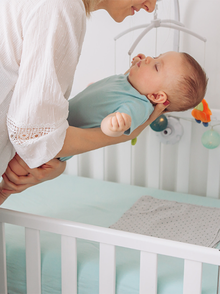 mother putting sleeping baby in crib