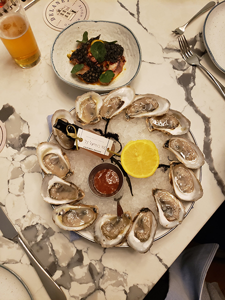 photo of a plate of a dozen oysters, with lemon, cocktail sauce, a salad and a beer