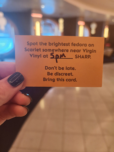 Photo of Amy's hand holding a card that says "Spot the brightest fedora on Scarlet somewhere near Virgin Vinyl at 5 pm SHARP. Don't be late. Be discreet. Bring this card."