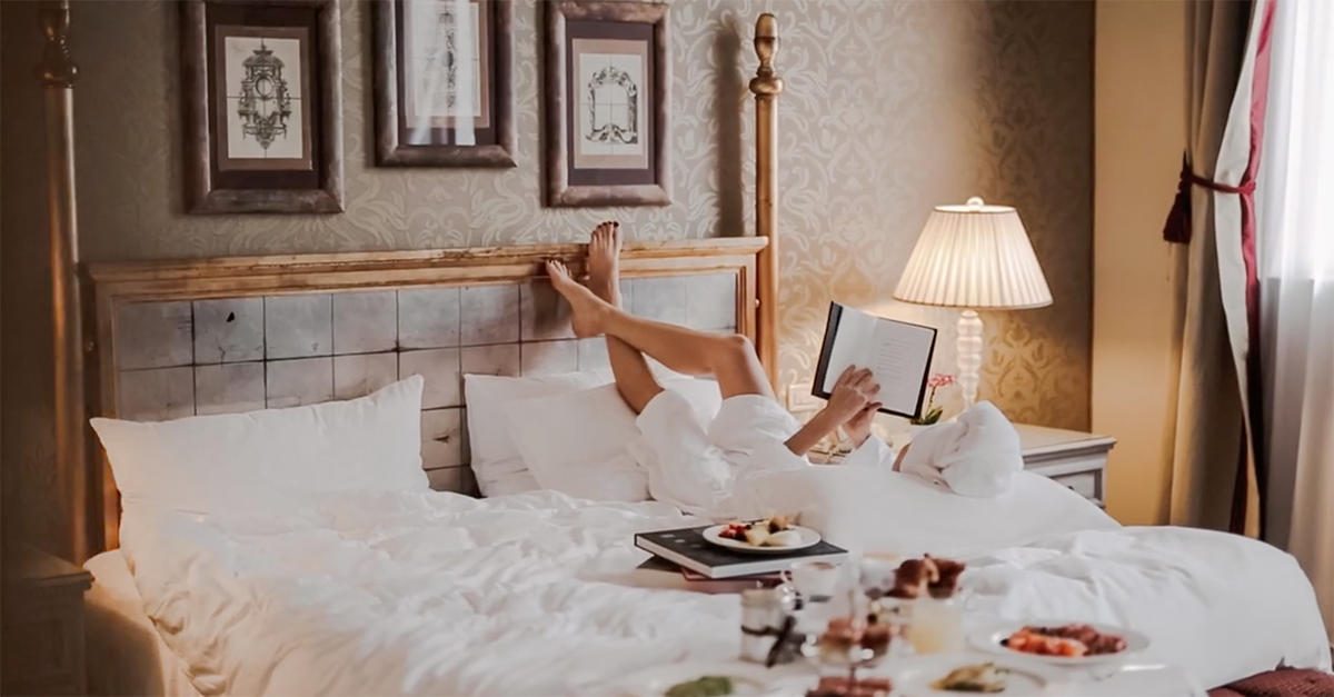 woman relaxing in luxury hotel in a bath robe on bed with a book