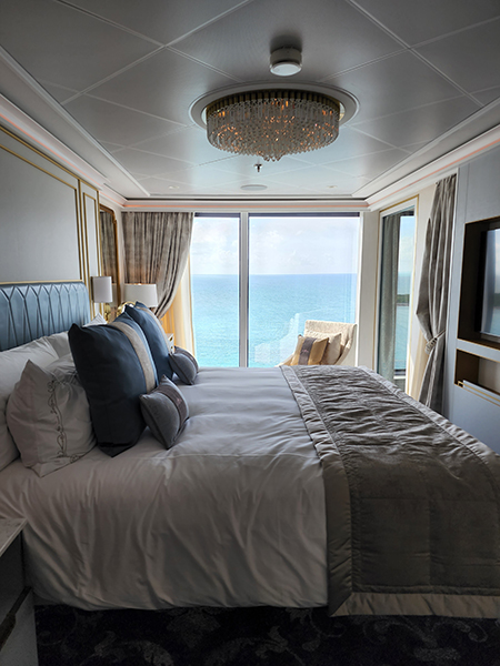 photo of a stateroom on board Disney Cruise lines, showing an elegant bed with a large window behind it, overlooking the ocean