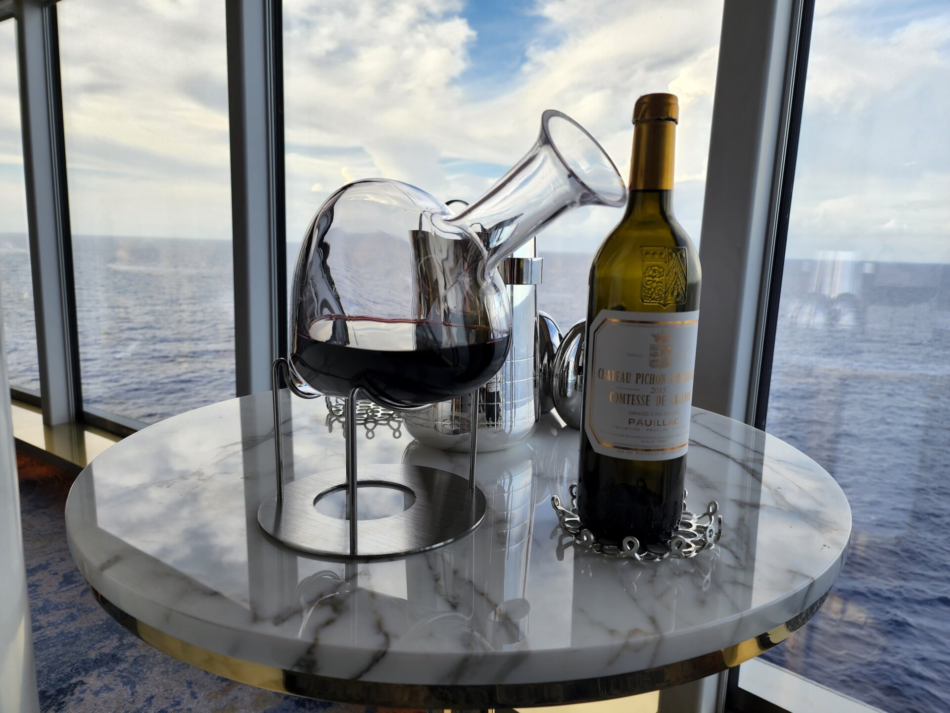 photo taken on board a Disney Cruise Line ship, of a bottle of red wine next to a glass decantur containing some of the wine, with a view of the ocean behind it.